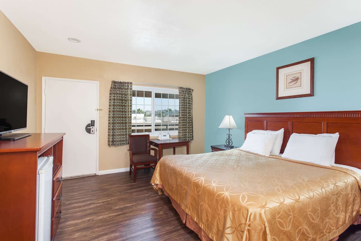 A hotel room with a bed, a desk, a chair, a television, and a window with curtains.