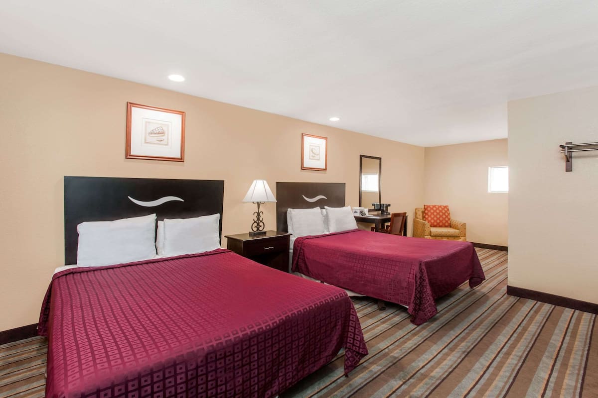 A hotel room with two beds, a chair, a desk, and framed pictures on the wall.