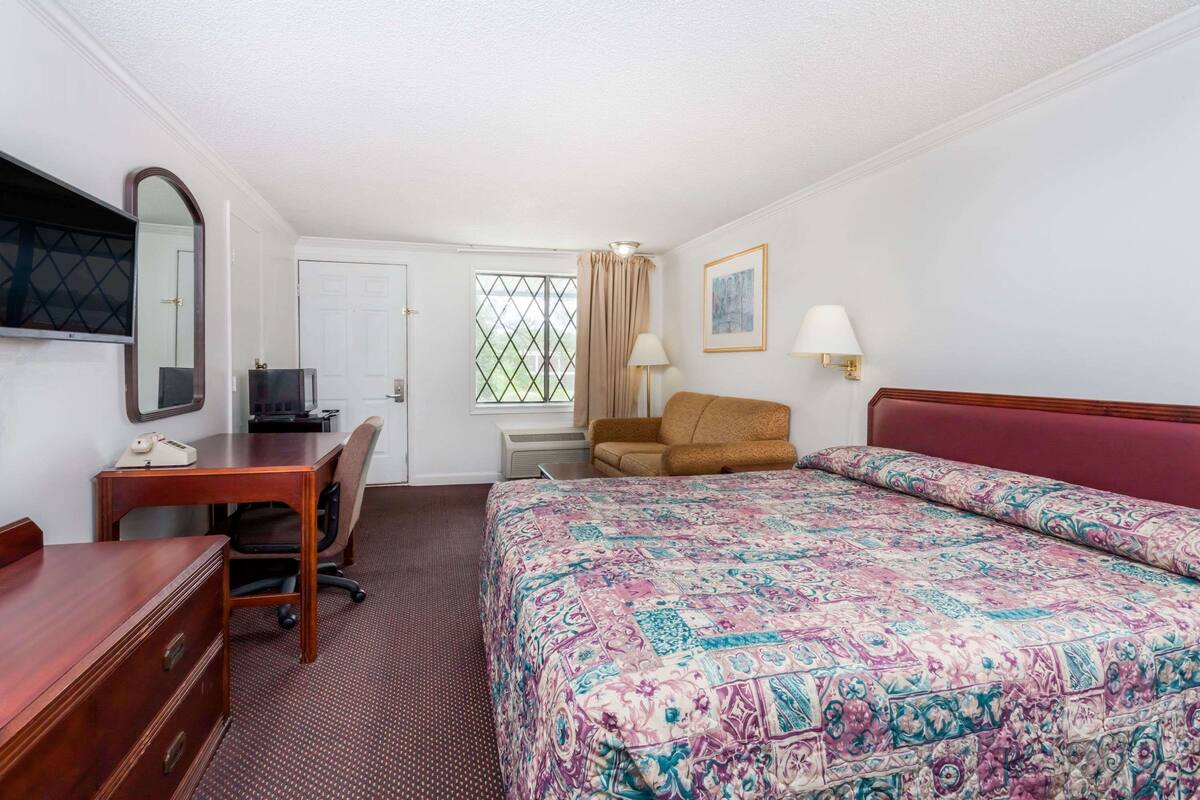 Une chambre d’hôtel comprenant un lit, un bureau, une chaise, une télévision, une fenêtre avec des rideaux et une porte.