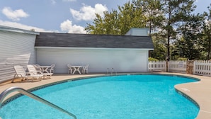 A swimming pool with a metal ladder, surrounded by lounge chairs and a covered area. - Knights Inn Columbia (Columbia)