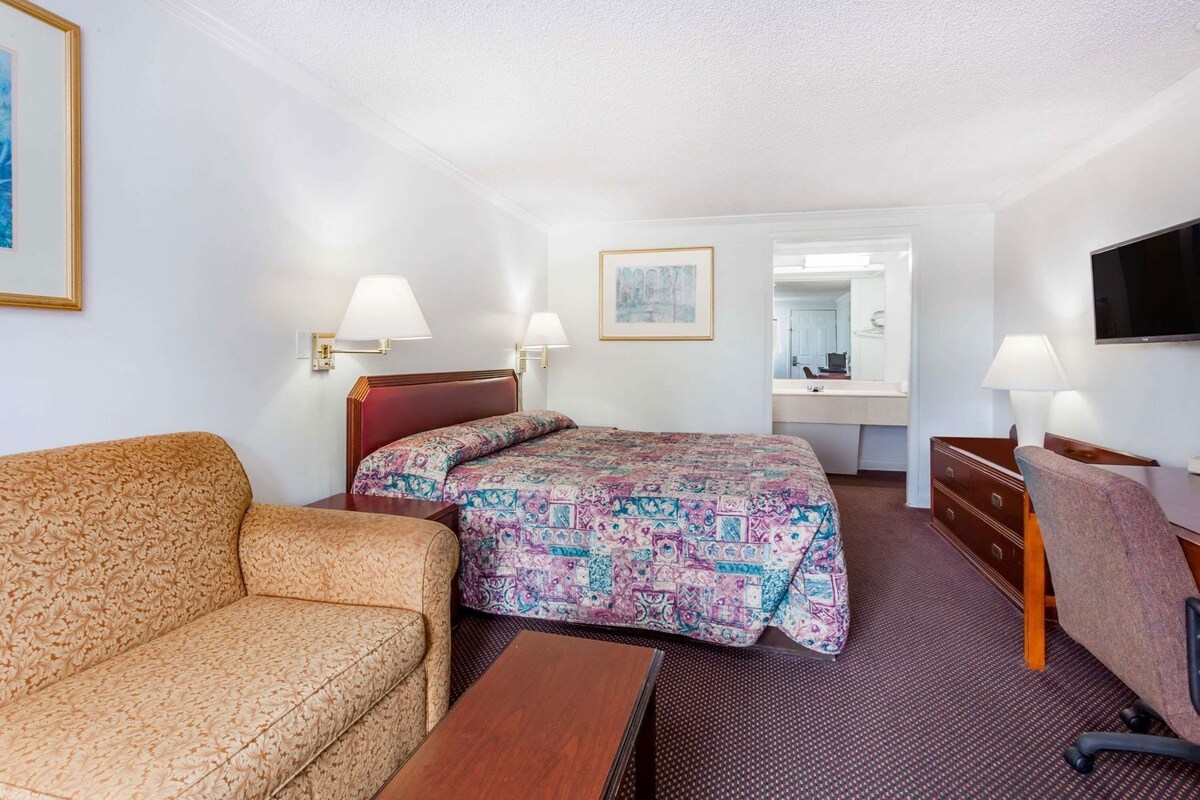 A hotel room with a bed, a sofa, a desk, and a television.