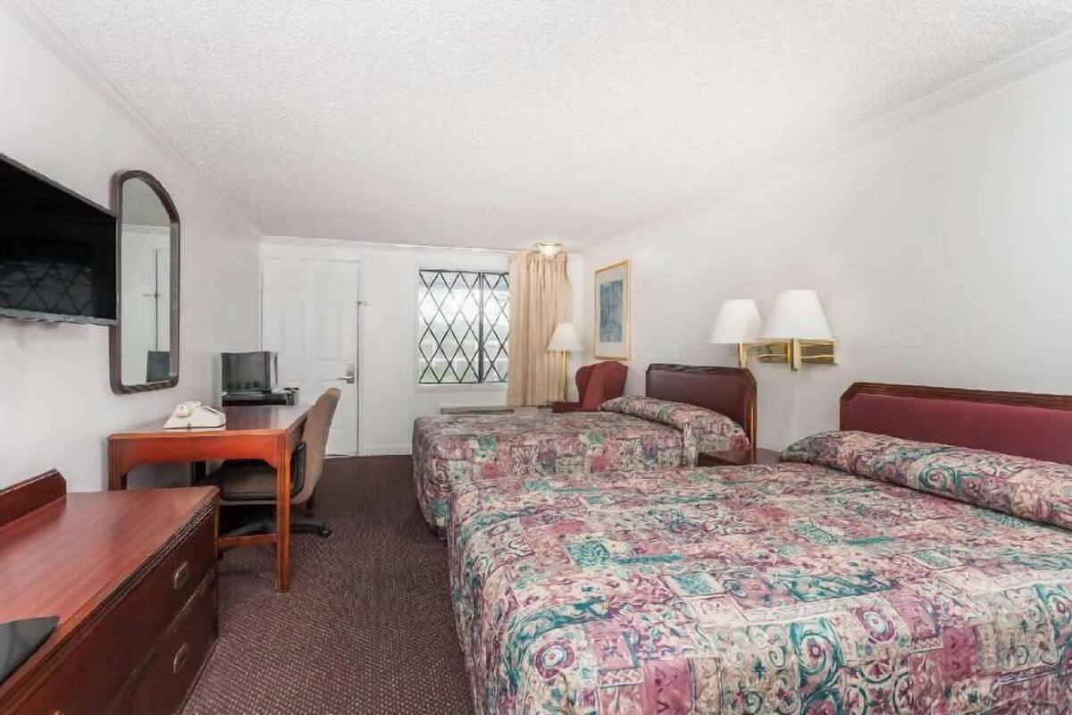 Une chambre d’hôtel équipée d’un bureau, de deux lits, d’un miroir, d’une télévision et d’une fenêtre avec des rideaux.