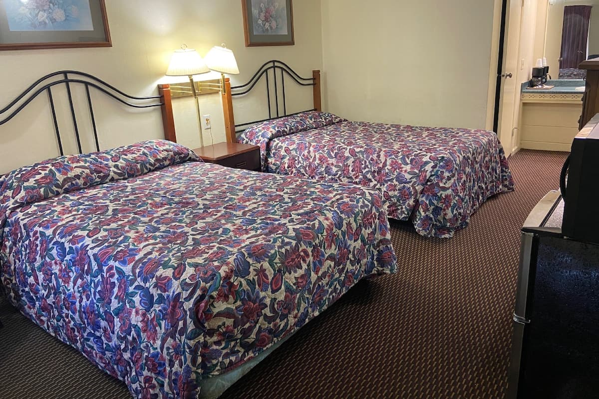 A hotel room with two beds, a desk, a chair, and a mirror.