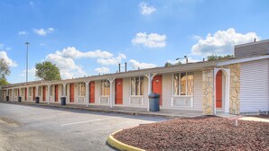 A row of motel rooms with individual doors, a parking lot, and a clear sky.