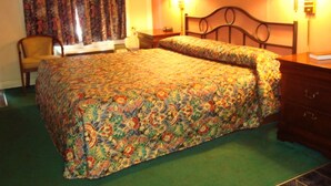 A hotel room with a bed, a chair, two bedside lamps, and a painting on the wall.