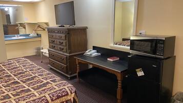 A hotel room with a bed, dresser, desk, microwave, and a mirror.