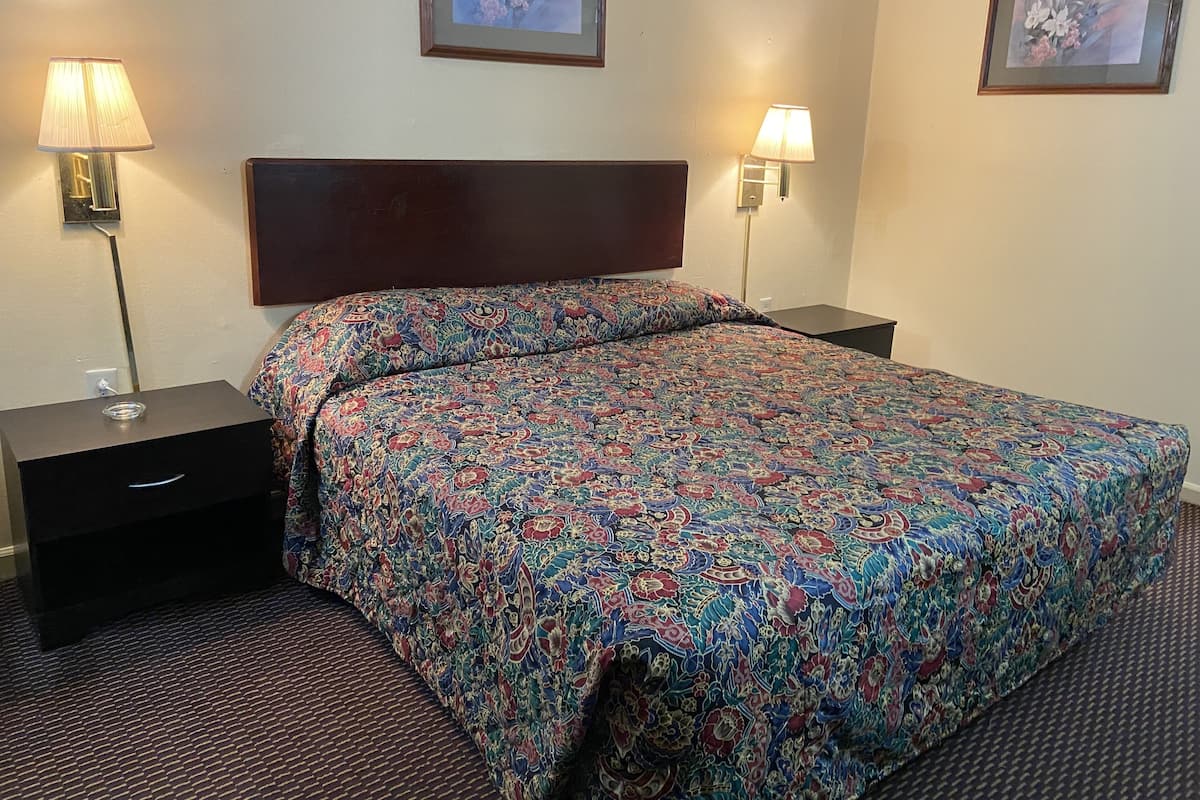 A hotel room with a large bed, two bedside tables, a nightstand, and two wall-mounted lamps.