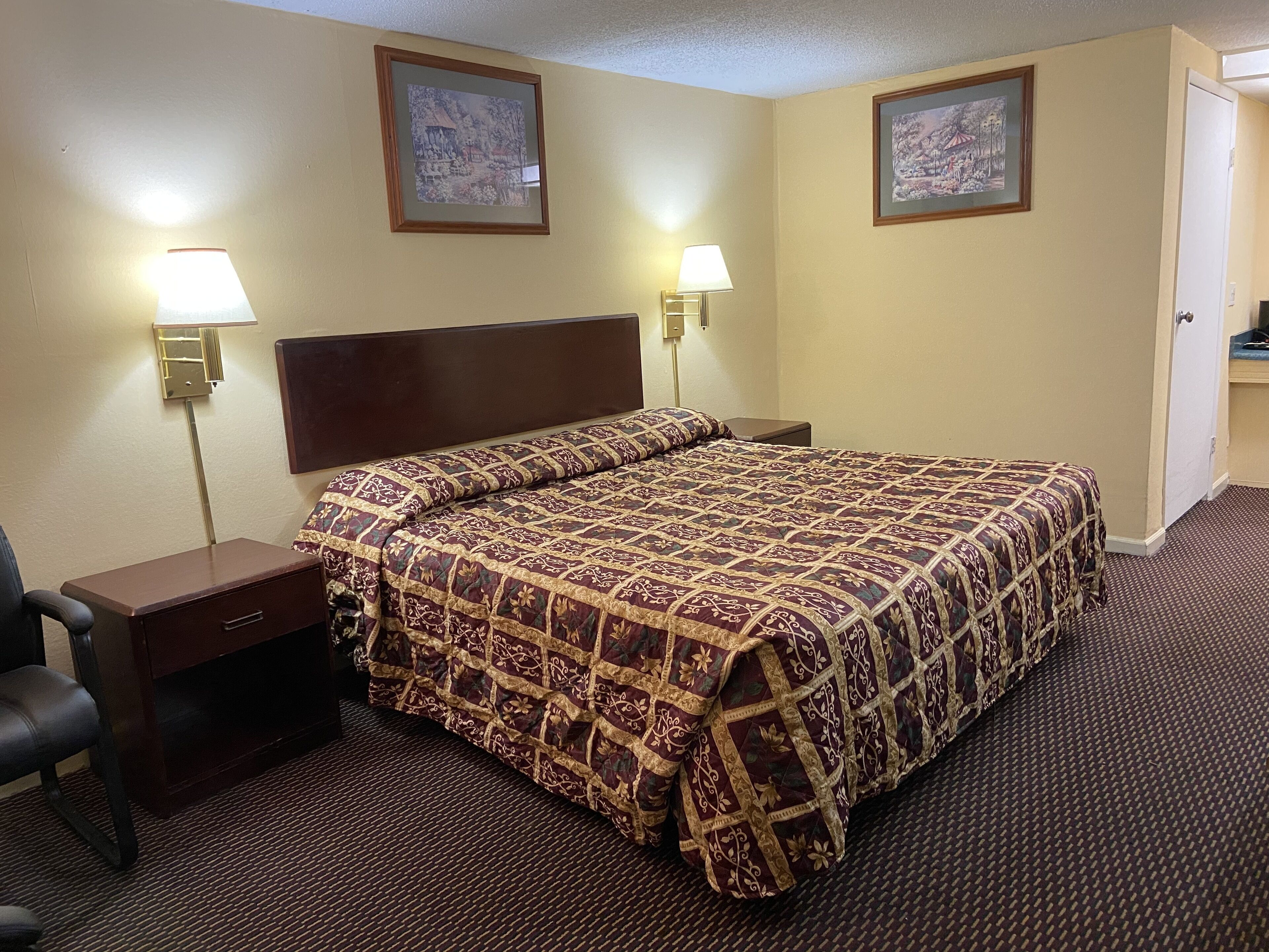 Camera d'albergo con un letto grande, due lampade ai comodini, una scrivania con una sedia e due quadri appesi alle pareti.