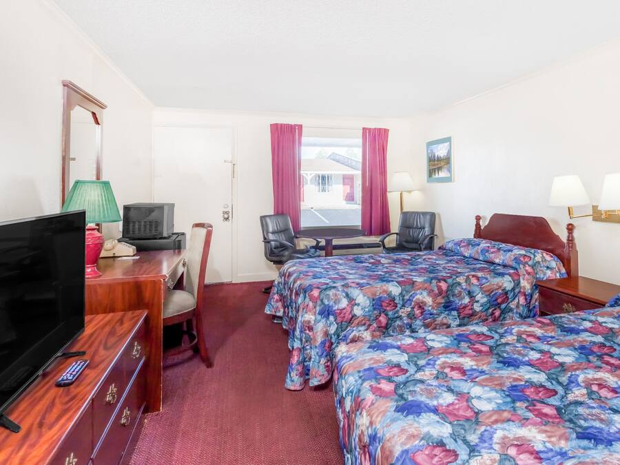 Habitación de hotel con dos camas, televisor, escritorio con lámpara y ventana con cortinas.