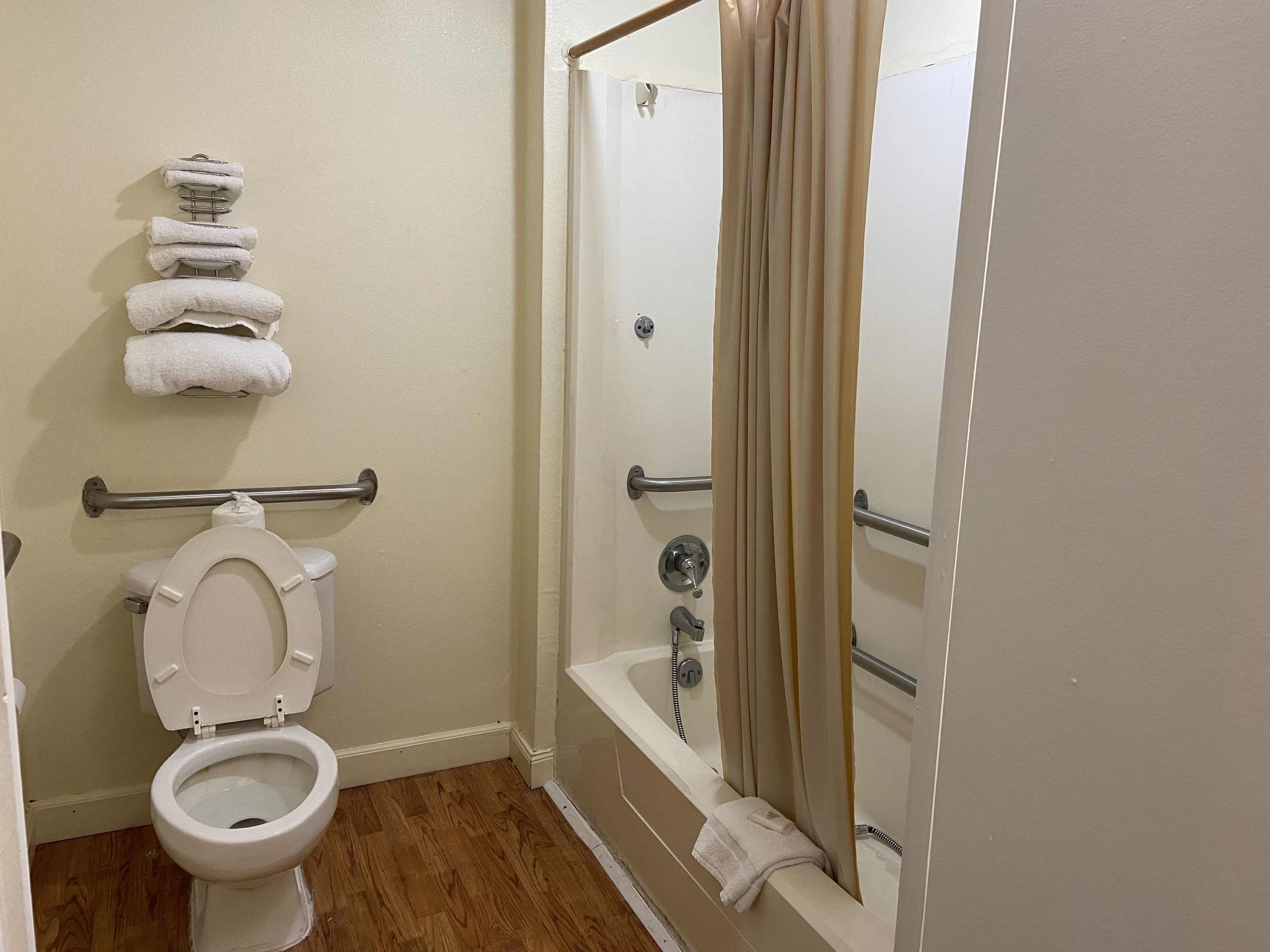 A bathroom with a toilet, a shower with a curtain, and a towel rack with folded towels.