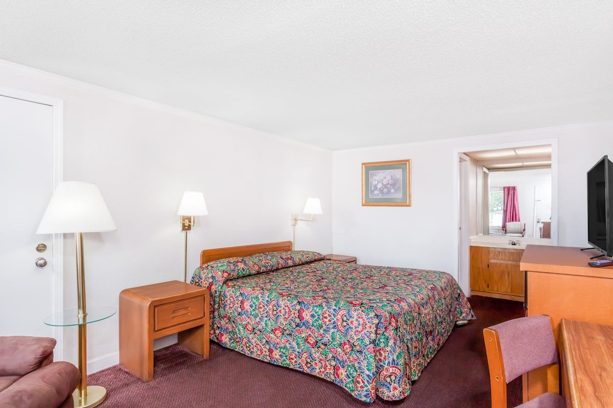 A hotel room with a bed, bedside tables, a desk, a chair, and a mirror.