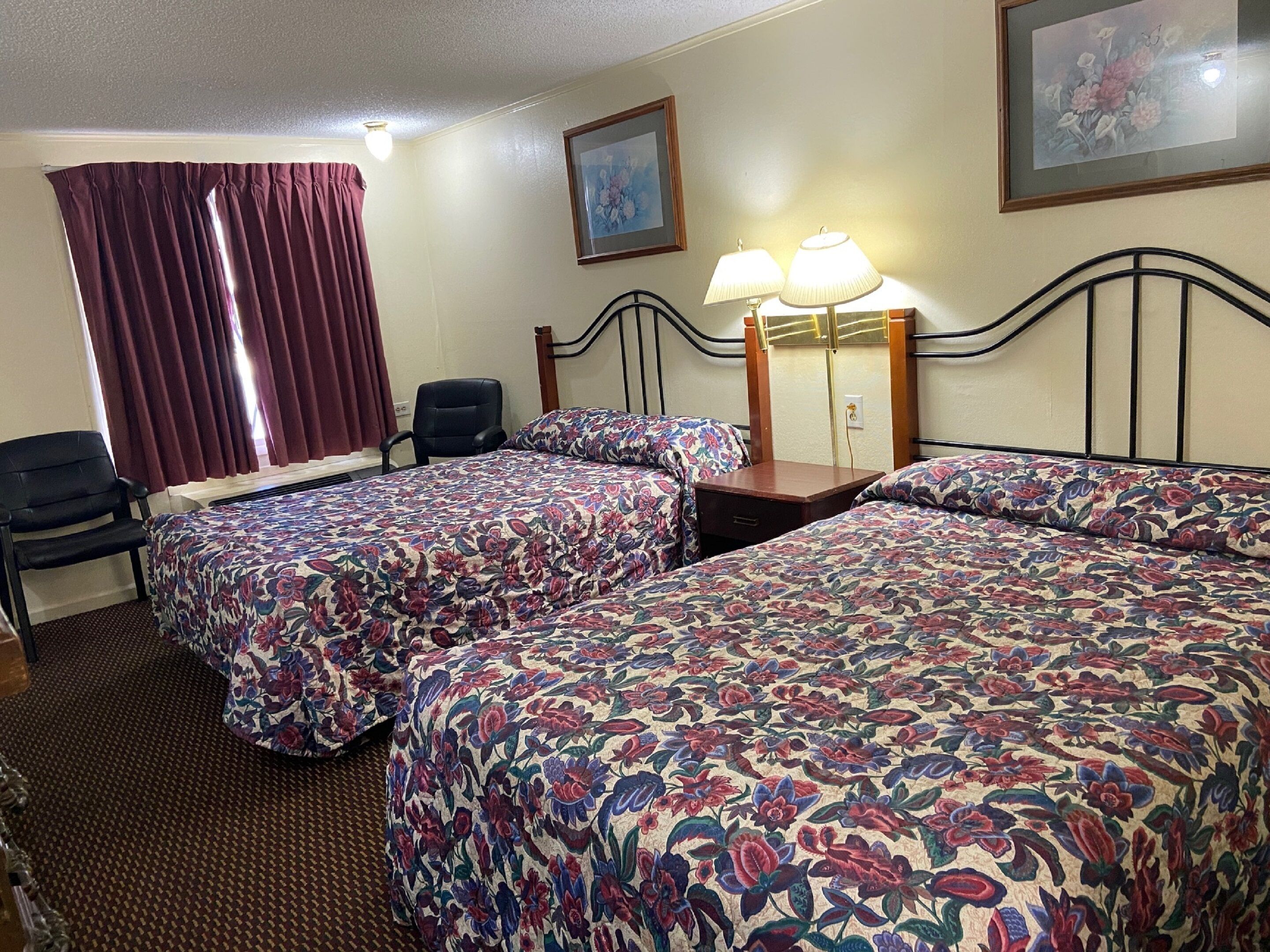 A hotel room with two beds, a desk, a chair, a lamp, and a painting on the wall.