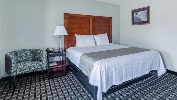 A hotel room with a bed, a chair, a nightstand, and a picture on the wall. - Travelodge by Wyndham Jackson I-40 Exit 82 (Jackson)