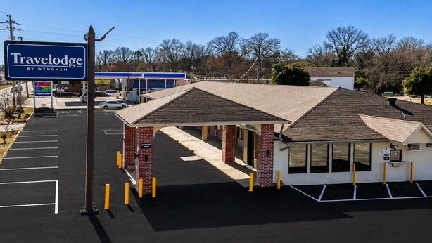 A Travelodge by Wyndham with a covered outdoor seating area, a gas station in the background, and a parking lot.