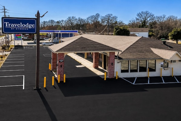 A Travelodge by Wyndham with a covered outdoor seating area, a gas station in the background, and a parking lot.