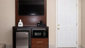 A compact kitchenette with a refrigerator, microwave, coffee maker, and a flat-screen TV mounted on a wooden wall. - Travelodge by Wyndham Jackson I-40 Exit 82 (Jackson)