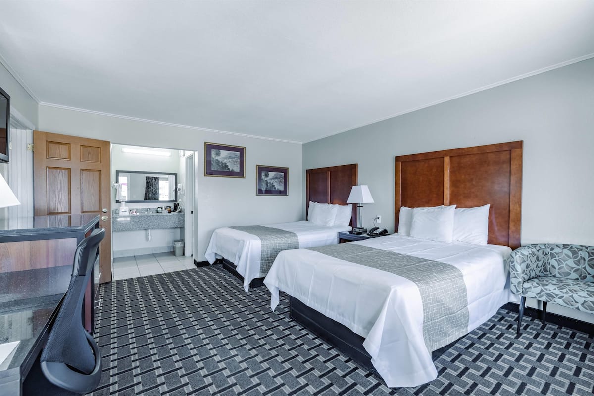A hotel room with two beds, a desk, a chair, a sofa, a bathroom, and a kitchenette.