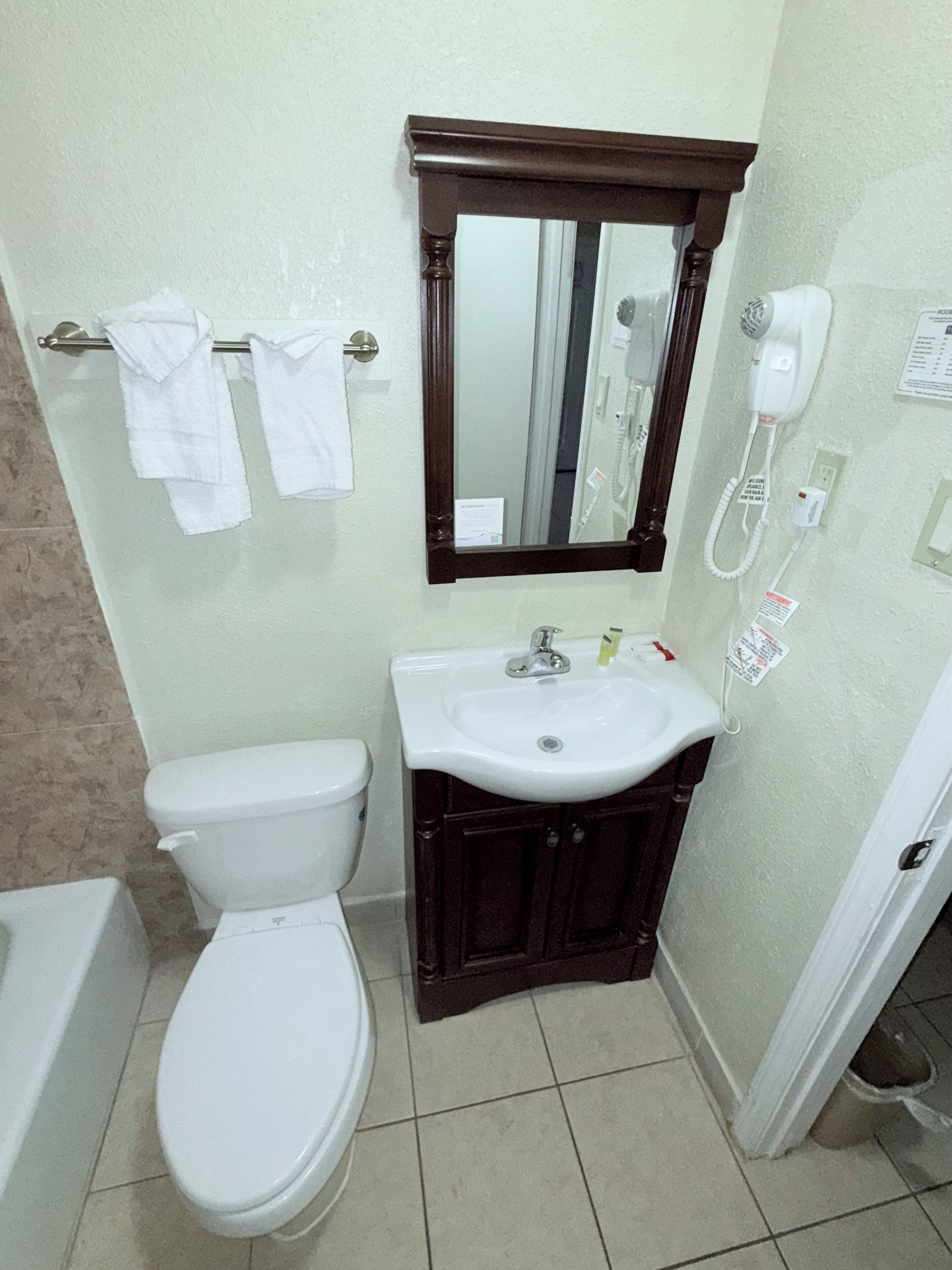 A bathroom with a white toilet, a sink with a mirror above it, and a hairdryer on the wall.