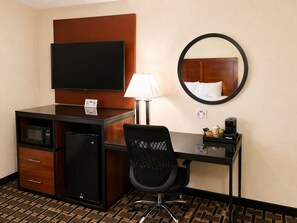 A hotel room with a desk, a television, a microwave, a coffee maker, a chair, a lamp, and a mirror. - Travelodge by Wyndham Jackson I-40 Exit 82 (Jackson)