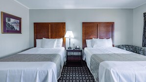 A hotel room with two beds, a nightstand with a lamp, a telephone, and a framed picture on the wall.