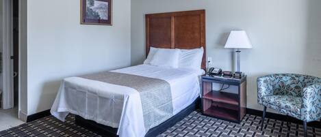 Habitación de hotel con cama, mesita de noche, lámpara, una silla y alfombra estampada.