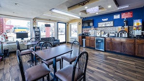 A restaurant interior with wooden flooring, tables, chairs, a kitchen area, and a large window with a view of the outside. - Travelodge by Wyndham Jackson I-40 Exit 82 (Jackson)