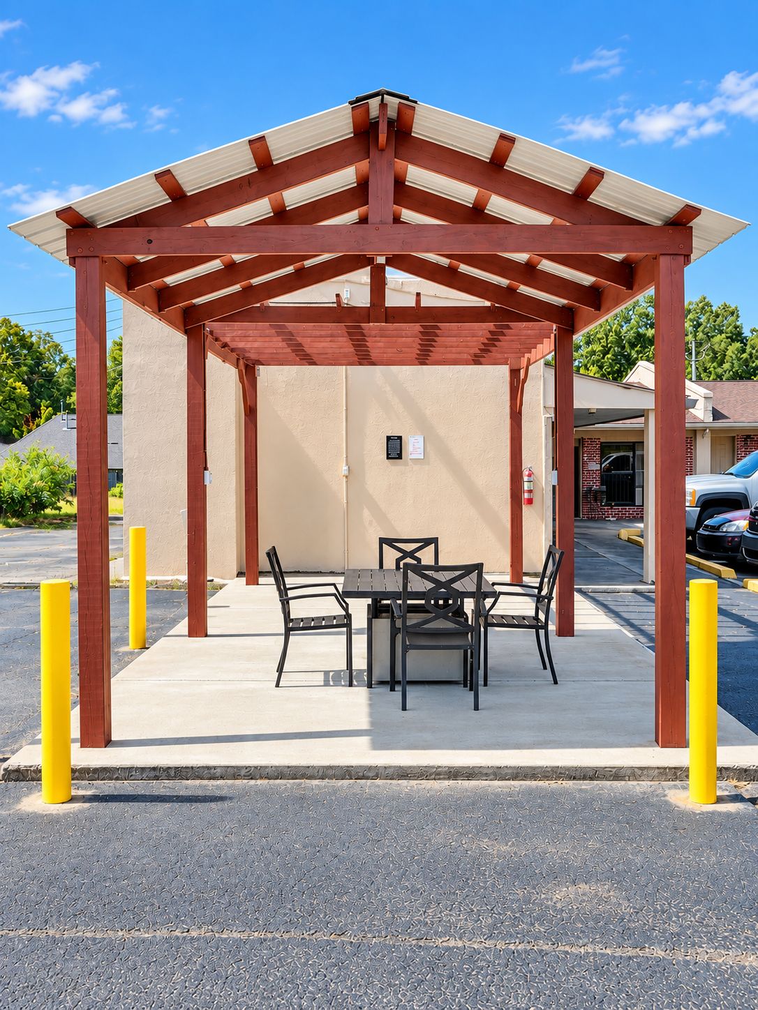 A covered outdoor seating area with a table and chairs, a building entrance, and a parking lot.