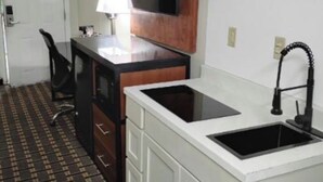 A compact kitchen with a built-in sink, a small dining area with a chair, and a television mounted above the counter. - Travelodge by Wyndham Jackson I-40 Exit 82 (Jackson)