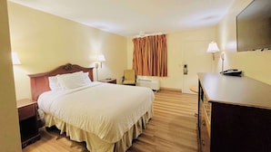 Ein Hotelzimmer mit einem großen Bett, Nachttischen, einem Schreibtisch, einem Sessel, einem Fernseher und einer Tür mit Vorhängen.