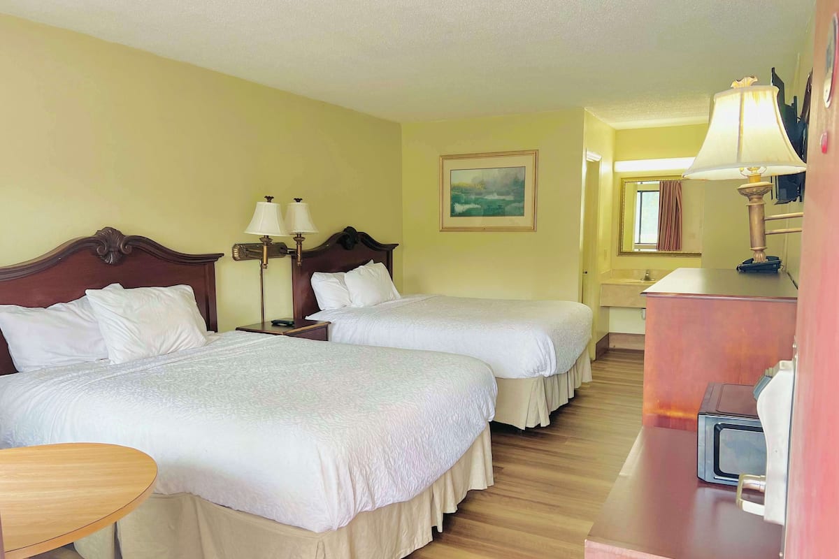 A hotel room with two beds, a wooden headboard, bedside lamps, a painting on the wall, and a desk with a lamp.