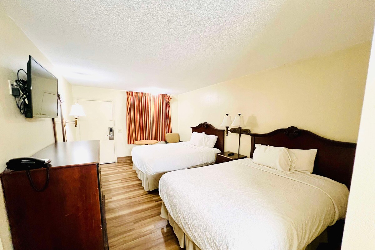 A hotel room with two beds, a desk with a telephone, a lamp, and a television mounted on the wall.