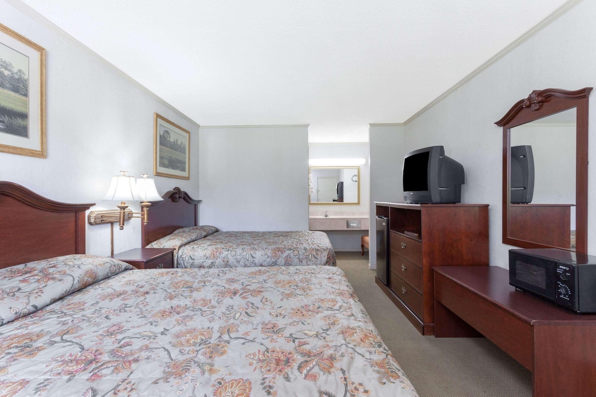 A hotel room with two beds, a desk with a television, a mirror, and a dresser.