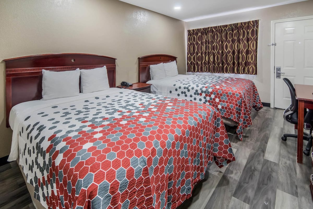 Ein Hotelzimmer mit zwei Betten, jeweils mit einem gemusterten Überwurf, einem Holzkopfende, einem Schreibtisch und einem Stuhl.
