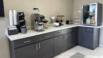 A modern kitchen area with a coffee machine, a refrigerator, and a beverage dispenser.