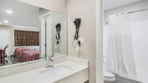 A bathroom with a white sink, a mirror, a hairdryer mounted on the wall, a toilet, and a shower curtain. - Super 8 by Wyndham Waco North I-35 (Waco)