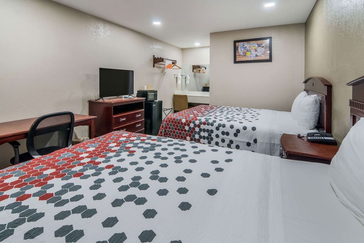 Ein Hotelzimmer mit zwei Betten, einem Schreibtisch, einem Fernseher und einem kleinen Tisch mit einem Telefon.