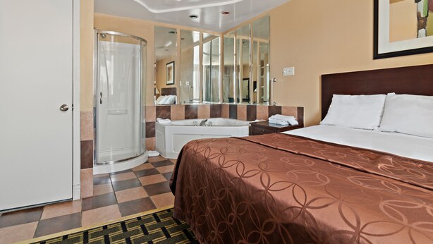 Una habitación de hotel con una cama, ducha, espejo de baño y puerta.