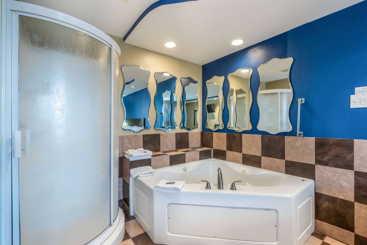 A bathroom with a large bathtub, a shower, and multiple mirrors on the wall.