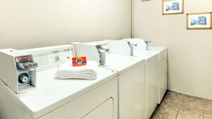 Zona de lavandería con varias lavadoras y una caja de detergente Tide.