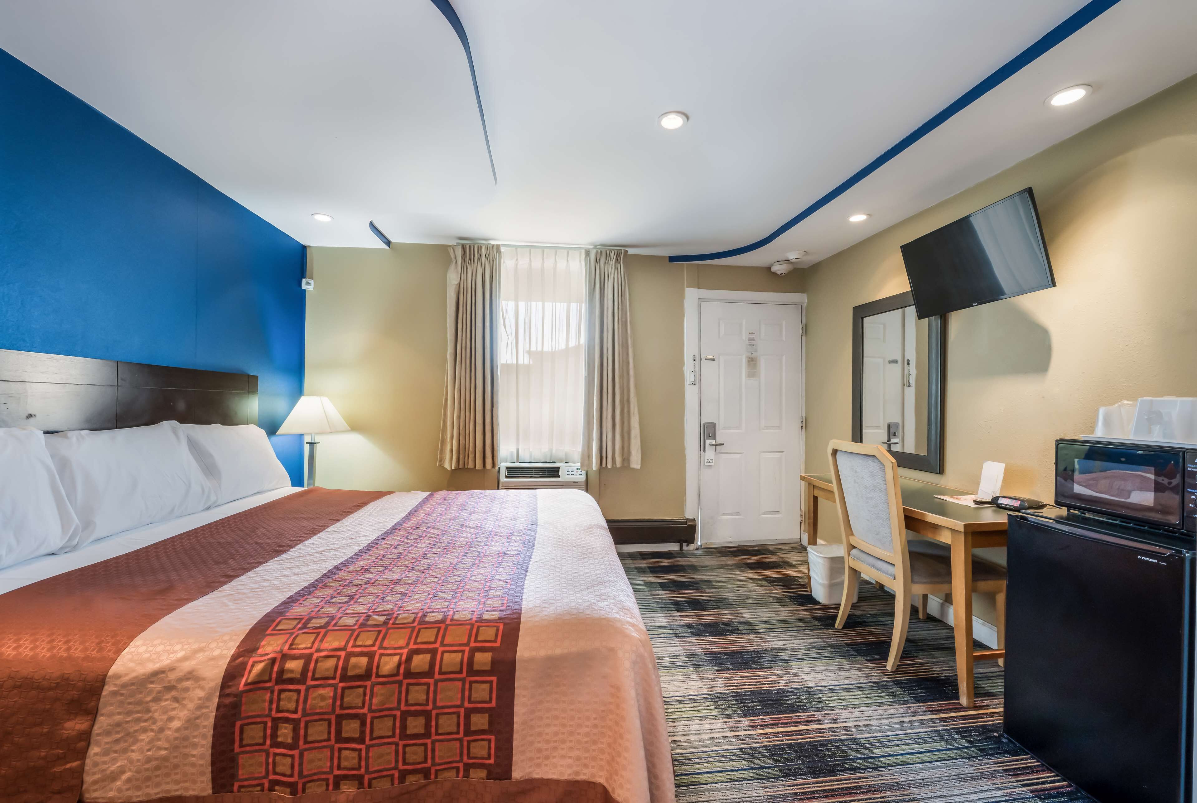 Ein Hotelzimmer mit einem großen Bett, einem Schreibtisch mit Stuhl, einem Fernseher und einer Tür.