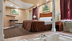 A hotel room with a large bed, a bathtub, a desk, and two chairs.