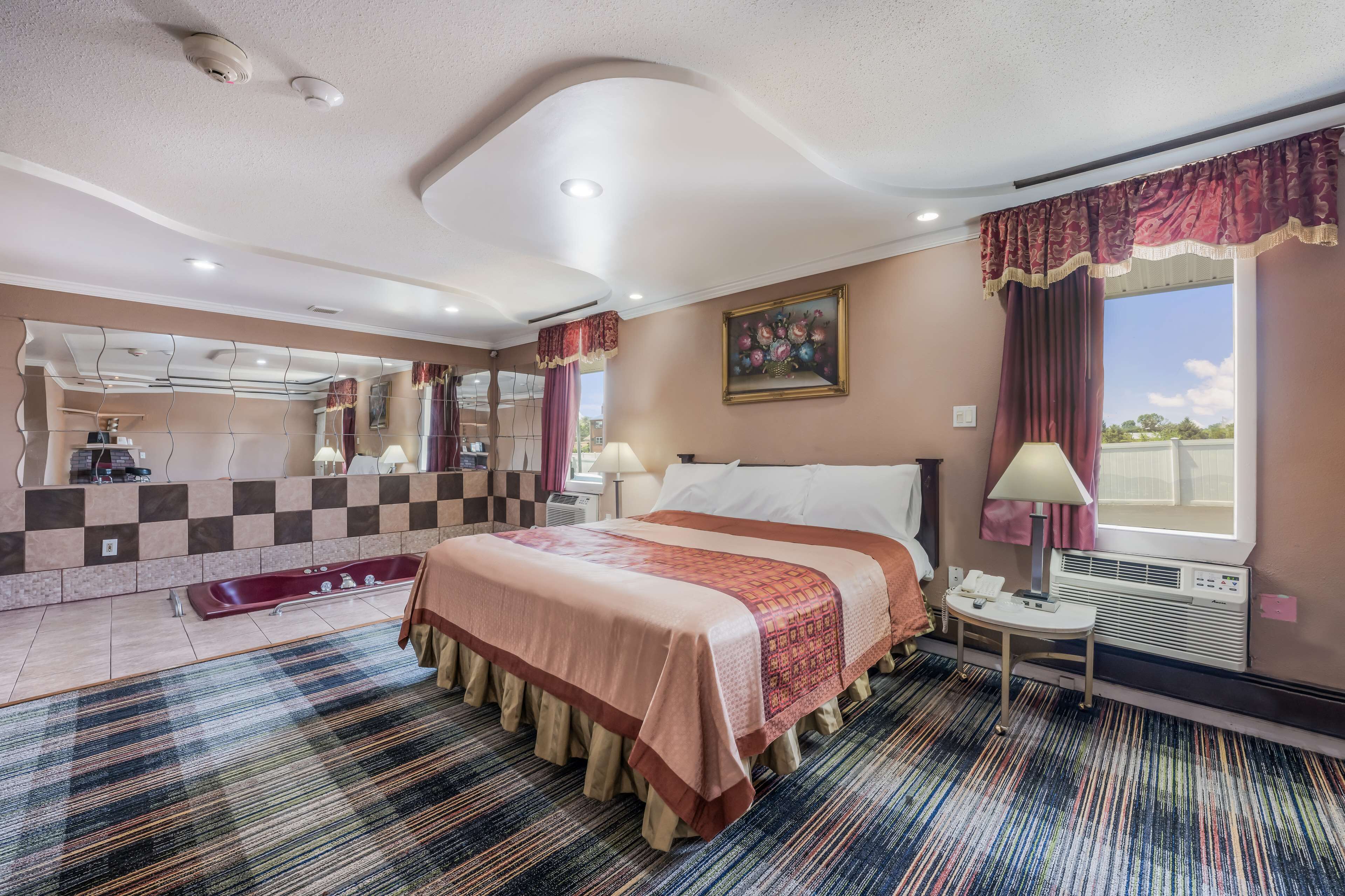 A hotel room with a large bed, a bathroom with a bathtub, a window with a view, and a painting on the wall.