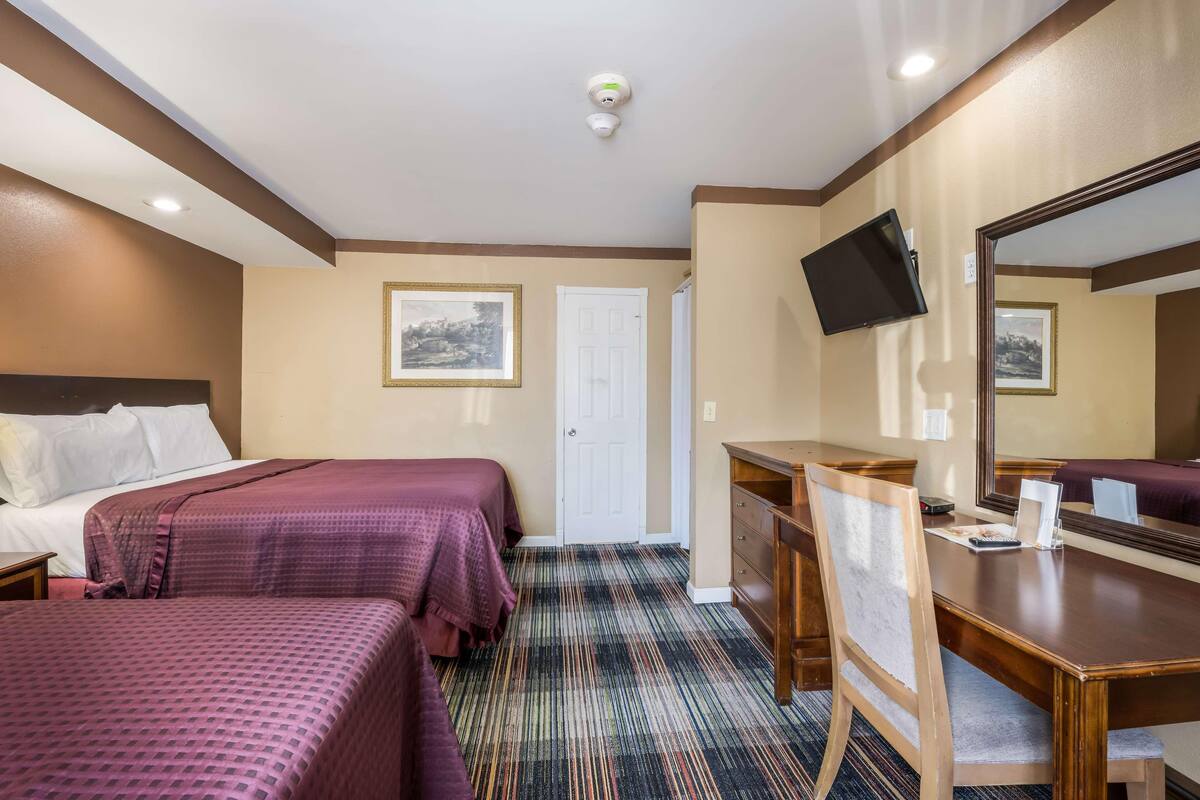 A hotel room with two beds, a desk, a chair, a television, and a mirror.