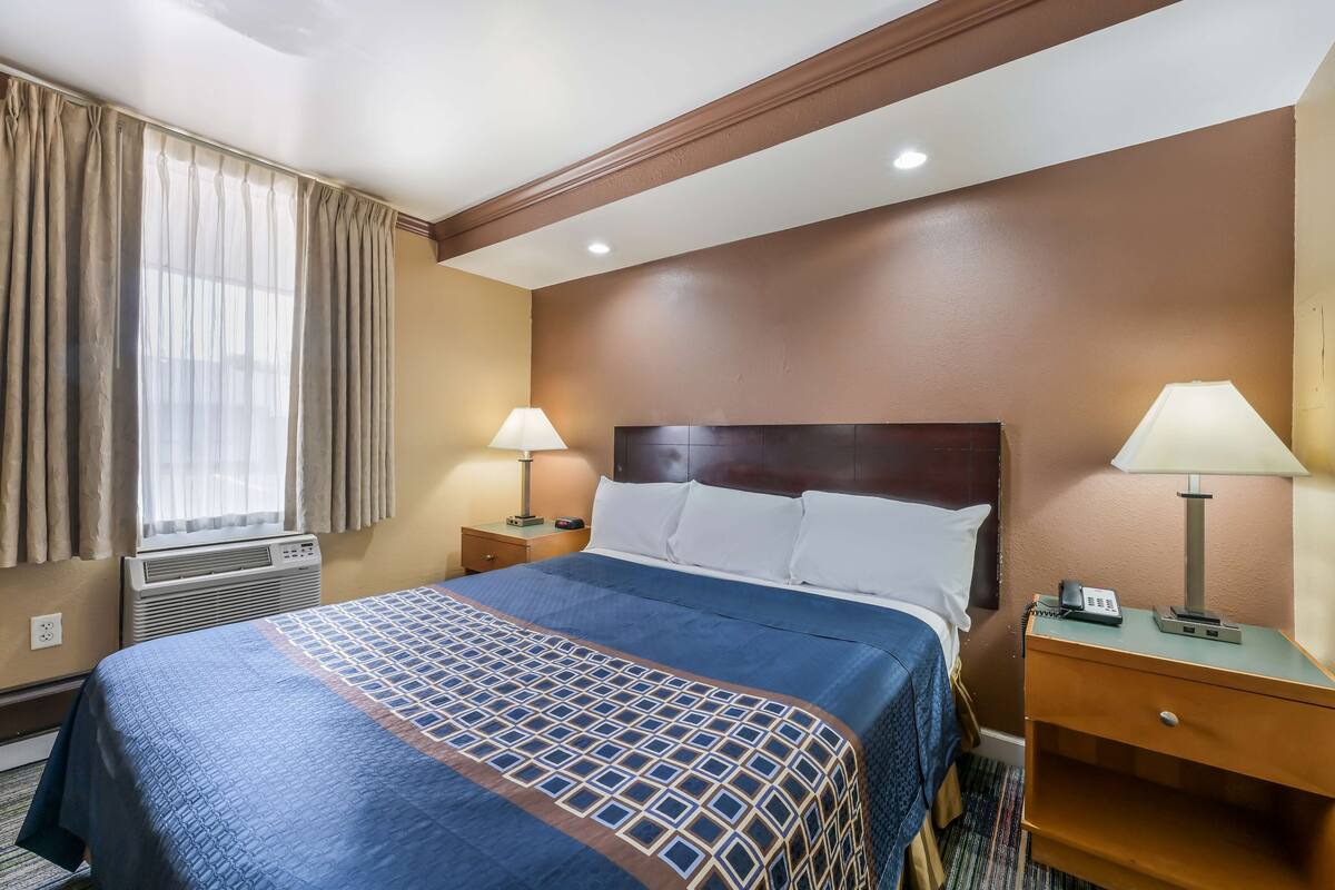 A hotel room with a bed, two bedside lamps, a nightstand, and a window with curtains.