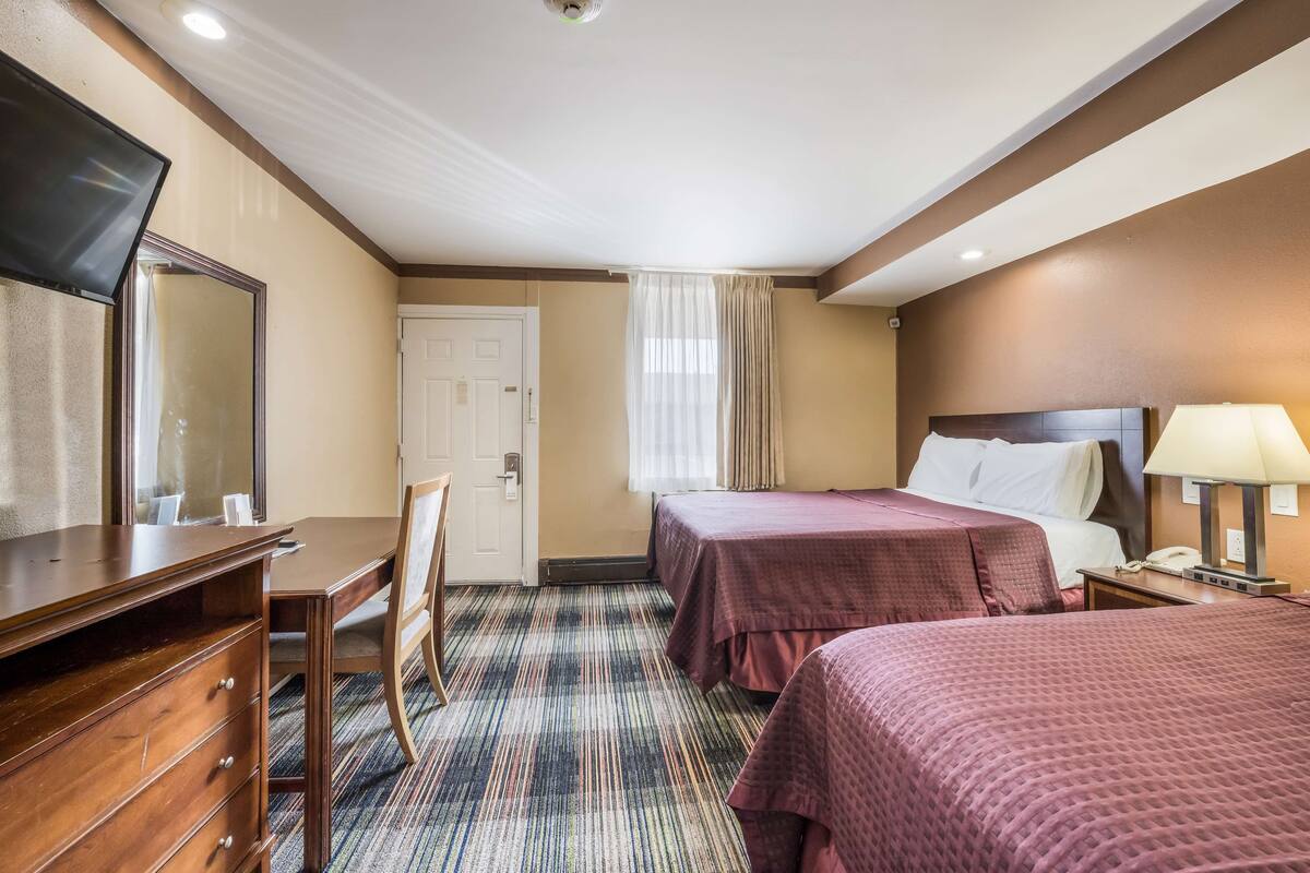 A hotel room with two beds, a desk with drawers, a chair, a TV, a lamp, and a door.