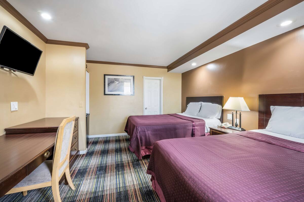 A hotel room with a desk, two beds, a TV, and a door.