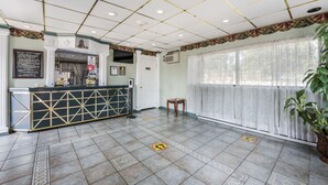 A reception area with a tiled floor, a reception desk, a wall-mounted air conditioner, and a large window with sheer curtains.