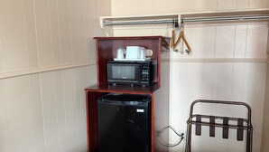 Una habitación compacta con kitchenette, que incluye microondas, refrigerador y un estante pequeño.