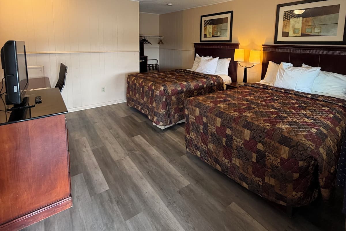 A hotel room with two beds, a desk, a TV, and a lamp.