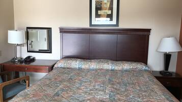 A hotel room with a bed, a desk, a chair, a telephone, a lamp, and a framed picture on the wall.